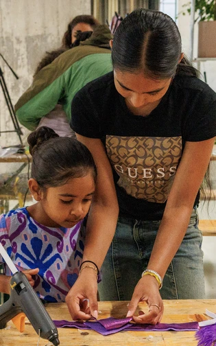 A child and instructor make a colorful carnival accessory together during a creative workshop.