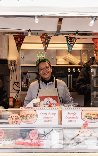 Three people serve food from a colourful African Food Festival stall.