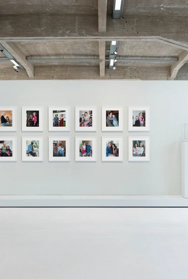 Een moderne tentoonstellingszaal waar je recht op een muurtje kijkt met in een grid foto's