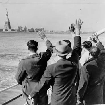 Zwaaiende mensen aan boord van een schip in New York, USA. Met op de achtergrond het Vrijheidsbeeld.