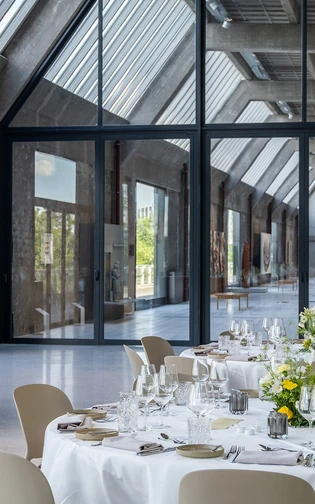 een formeel gedekte tafel met uitzicht op de tentoonstellingzaal, waar een auto te zien is