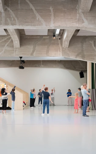 In een grote, moderne, loodsachtige ruimte beoefenen een groep mensen tai chi.
