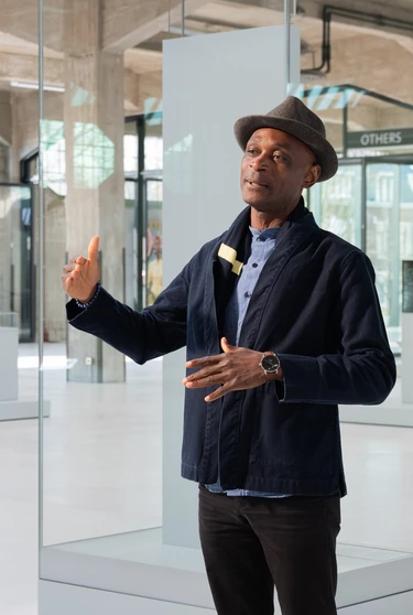 A person stands in Fenix, gesturing while speaking. They wear a hat and dark jacket.