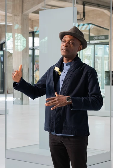 A person stands in Fenix, gesturing while speaking. They wear a hat and dark jacket.