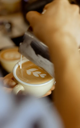 Barista creating intricate latte art with frothed milk, forming a delicate leaf pattern on coffee