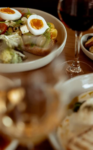A table set for a meal featuring a plate of salad with eggs and vegetables, a glass of red wine,