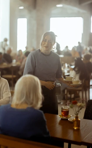 A friendly server in a cozy cafe approaches a table with two older women.