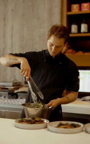 Chef in a black uniform focused on preparing a salad in a modern kitchen.
