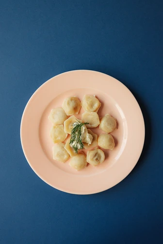Plate of dumplings arranged in a circle with a garnish of dill and sour cream