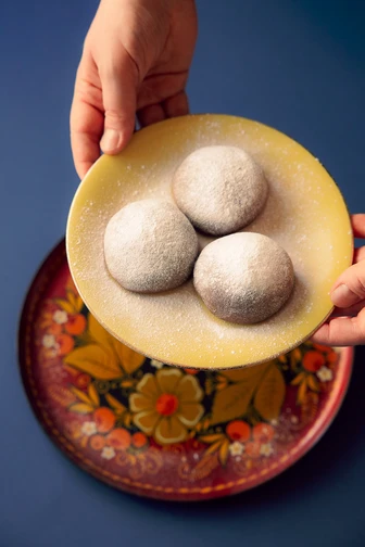 Hands holding a yellow plate with three sugar-dusted cookies above a floral-patterned plate