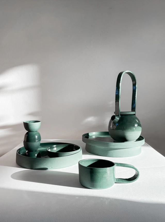 A collection of green glazed ceramic tableware, including cups, trays and a sculptural teapot.