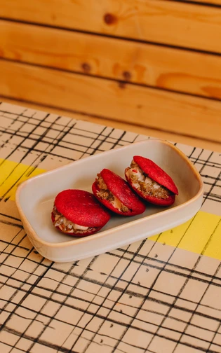 drie kleine rode broodjes gevuld met vlees in een bakje op een gestreepte tafel