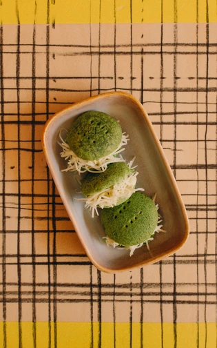 drie kleine groene broodjes gevuld met avocado en kaas in een bakje op een gestreepte tafel
