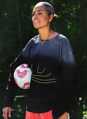 A woman in sportswear holds a football under her arm while standing outdoors.