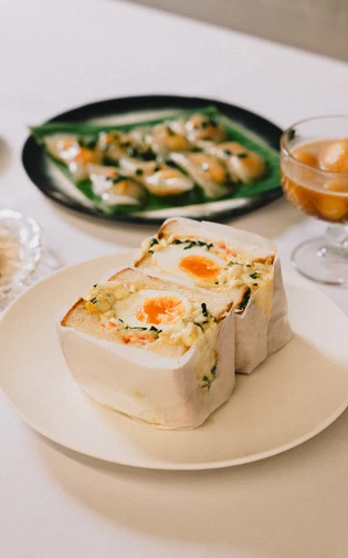 A neatly arranged table features two egg sandwiches, a plate of dumplings, and a dessert glass.