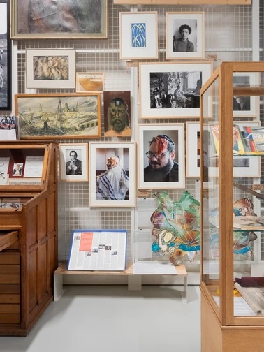 een kunstdepot met foto's en schilderijen aan een wand, en verschillende vitrines met objecten